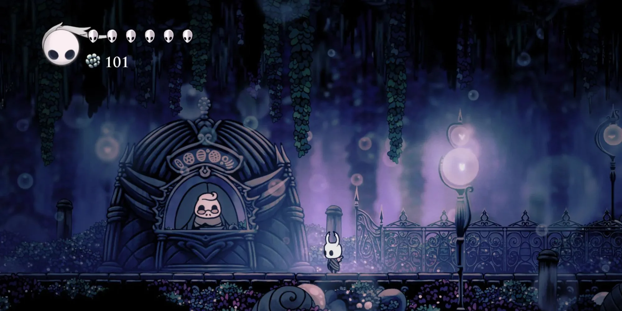 Millibelle, một nhân vật hình bọ cánh cứng trong Hollow Knight, đang đứng cạnh một quầy giao dịch ngân hàng làm từ vỏ sò